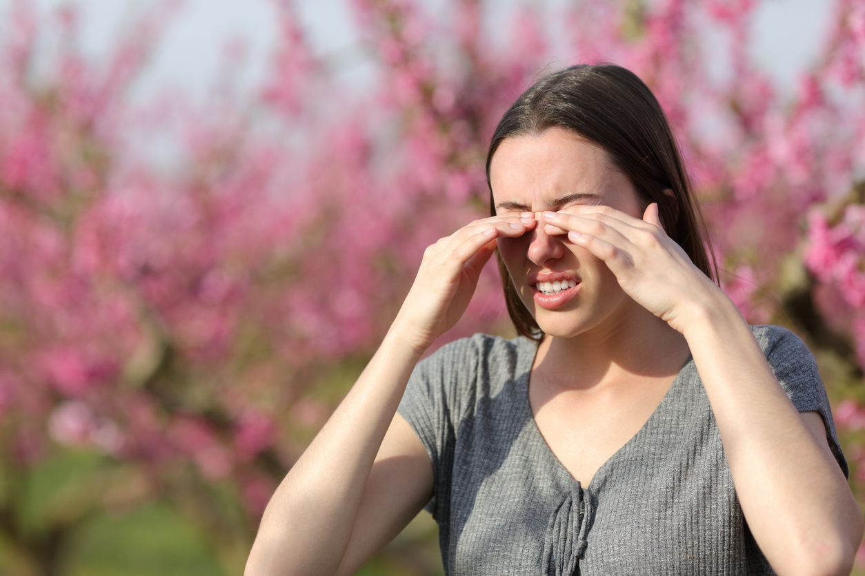 Woman rubbing her itchy, irritated eyes outdoors during spring pollen season