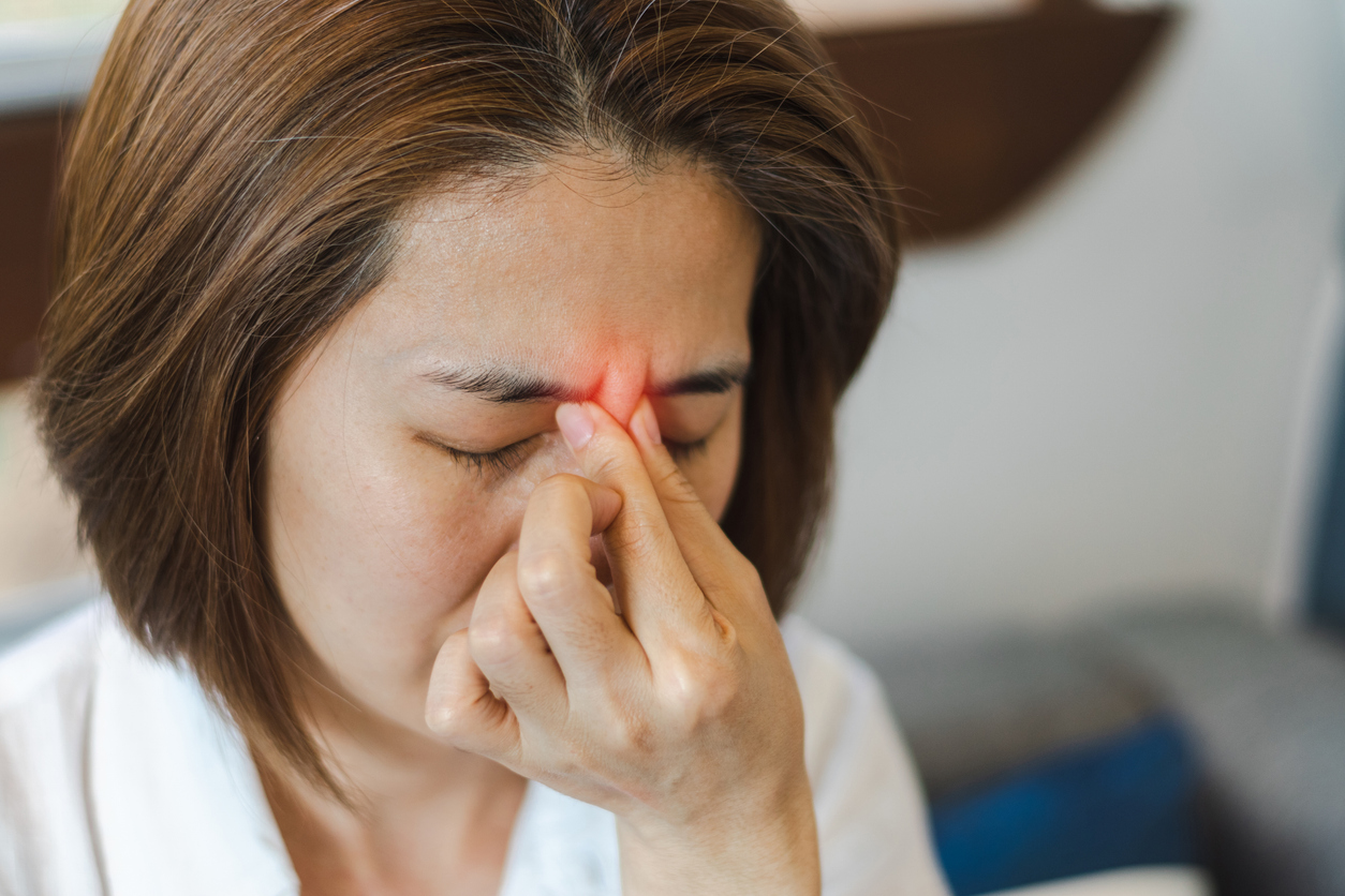 Woman pinching the bridge of her nose from chronic sinusitis facial pressure and headache